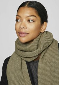 Khaki-ribbet strikket tørklæde, svøbt om halsen, lavet af blødt stof, med et struktureret mønster og en pæn finish, suppleret af en mørk sweater under.