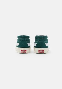 Grüne Wildleder High-Top Sneaker mit weißen Streifen, gepolstertem Kragen und Gummisohlen. Rotes Logo an der Ferse.