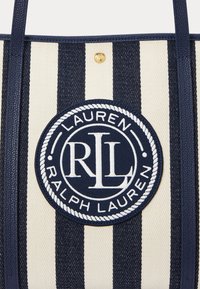Tote torba v mornarsko modri in kremni črtasti zasnovi s krožno tkaninsko nalepko, ki vsebuje bel logotip "Ralph Lauren", na vrhu pa je zlata okrogla dodatna oprema.