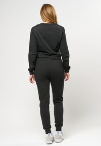 Svart, långärmad sweatshirt och matchande joggers i mjukt material. Joggers har smalnande ben och elastiska muddar. Minimalistisk design.