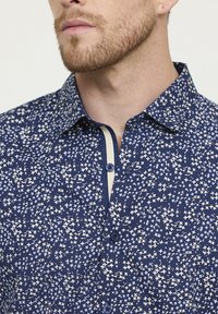 Chemise marine présentant un motif d'étoiles en crème et bleu clair. Fermeture à boutons à l'avant avec un col contrasté et des accents de boutons. Matériau en coton.