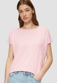 Rosa T-Shirt mit kurzen Ärmeln und Rundhalsausschnitt, aus weichem Stoff gefertigt. Verfügt über eine lockere Passform und dezente Drapierung. Kombiniert mit hellblauen Jeans.