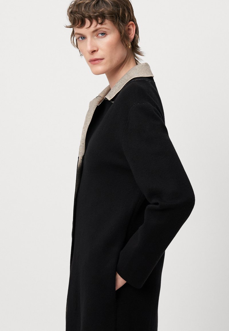 Cappotto nero con un colletto beige texturizzato, maniche lunghe, tasche laterali e una silhouette dritta. Tessuto morbido con un design pulito e minimalista.