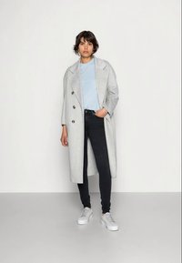 Casaco cinza-claro de dupla face, t-shirt azul, jeans skinny pretos e ténis brancos. Textura suave e design minimalista.