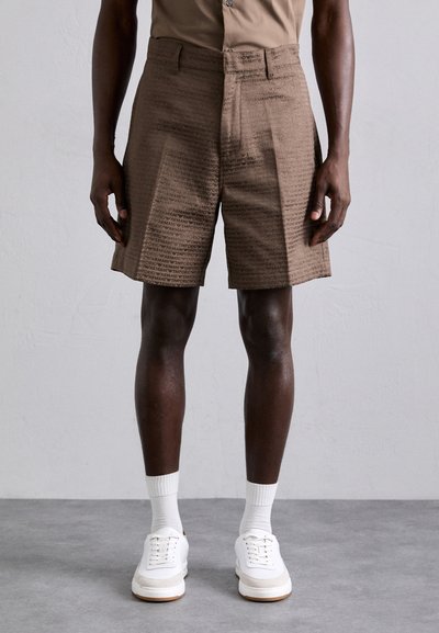Brown shorts with a textured pattern featuring the word "EMPORIO" in black. Made from a lightweight material, paired with white sneakers.