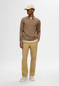 Beiger Langarmpullover mit Reißverschlusskragen, kombiniert mit hellkhakifarbenen Hosen und beigen Turnschuhen. Die Mütze ist ebenfalls beige. Einfaches, sauberes Design.