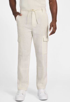 Pantalones cargo crema fabricados con un tejido ligero; cuentan con dos bolsillos frontales, cintura con cordón y bolsillos laterales; combinados con zapatillas blancas.