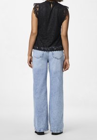 Top in pizzo nero con bordi scallop e apertura a chiave sul retro, abbinato a jeans in denim a gamba larga di colore azzurro chiaro con design classico a cinque tasche.