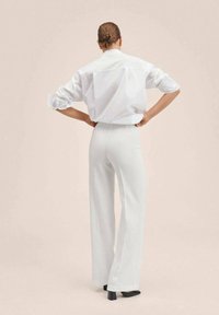 Chemise blanche surdimensionnée avec des manches roulées, associée à un pantalon blanc taille haute. Tissu lisse et coupe ajustée, avec des chaussures à talons noires.