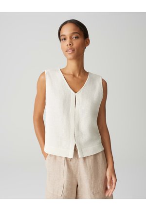 Ivory gebreid zonder mouwen top met een V-hals, gekenmerkt door een knoopsluiting aan de voorkant en een gestructureerd patroon. Gecombineerd met lichtbeige linnen broeken.