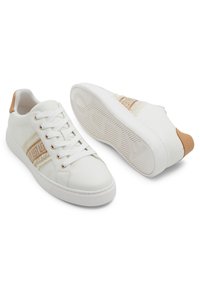 Low-top white sneakers with tan heel accents, braided beige and tan patterned side stripes, and white rubber soles with textured grip.