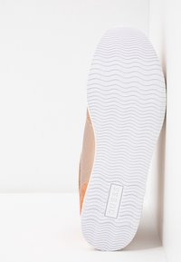 Baskets avec une tige texturée couleur tan, ornées d'accents orange et d'une semelle en caoutchouc blanche, affichant un motif de semelle ondulé. Logo de la marque sur la semelle.