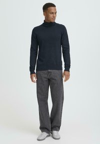 Námornícky rolákový sveter z mäkkej tkaniny; priliehavý strih s dlhými rukávmi. Kombinovaný s voľnými vyblednutými sivými džínsami a sivými teniskami.