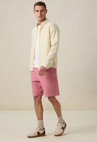 Chemise à rayures jaune clair sur un t-shirt blanc, associée à un short rose texturé et des baskets beiges avec des accents marron.
