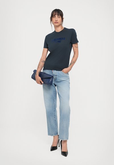 Donker marineblauwe T-shirt met korte mouwen met bedrukte logo, lichtblauwe rechte jeans en een gestructureerde blauwe clutch. Stiletto-hakken maken de look compleet.