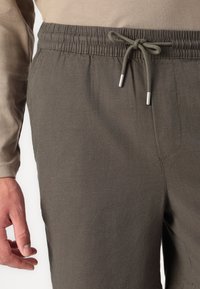 Pantalons de jogging vert foncé avec une taille élastique, fermeture à cordon de serrage et poches latérales, dotés d'un tissu doux et texturé.