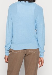 Ljusblått stickat tröja med ribbad textur, rund halsringning och långa ärmar. Bärs med bruna byxor med synliga sömnadsdetaljer.