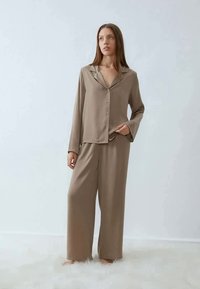 Beige to-delt pyjamasæt lavet af blødt stof; har en skjorte med knaplukning, krave og bukser med bred ben; minimalistisk design.