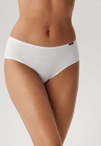 Białe bawełniane majtki hipsterki o gładkiej teksturze, bez widocznych szwów, z cienkim pasem i dyskretną metką logo na biodrze.