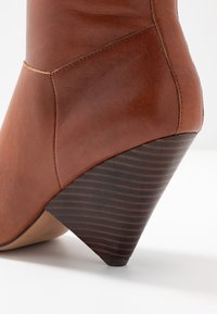 Bottine en cuir marron avec un talon conique texturé. Présente une surface lisse et des détails de couture subtils, se transformant en un talon foncé rayé.