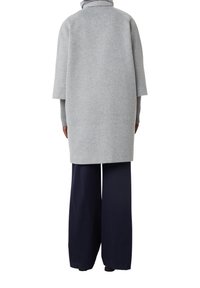Hellgrauer Wollmischung Oversized-Mantel mit kurzen Ärmeln, kombiniert mit marineblauen weit geschnittenen Hosen. Glatte Textur mit minimalen Nähakzenten.