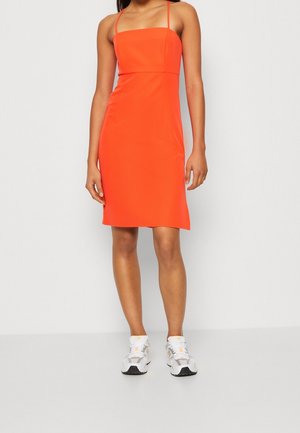 Robe rouge sans manches avec un décolleté carré, coupe moulante, longueur mi-cuisse, assortie à des chaussures de sport blanches et grises.