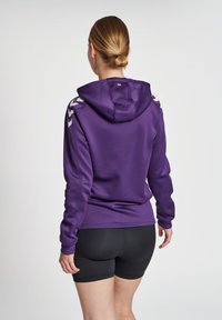 Felpa con cappuccio viola in tessuto liscio, con dettagli laterali bianchi e una vestibilità aderente, abbinata a pantaloni corti neri.