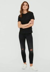 Black crew neck t-shirt paired with distressed black skinny jeans featuring knee rips and white sneakers. Simple, casual outfit.