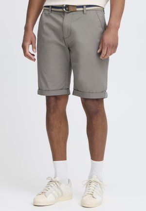 Shorts en coton gris avec ourlets retroussés, présentant un design à l'avant plat et une légère brillance, assortis à des baskets blanches et des chaussettes blanches.