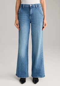 Light blue wide-leg jeans made from denim, featuring a high waist, side pockets, and a slightly faded finish. Paired with black heeled shoes.