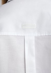 Witte shirt met een getextureerde stof, een verticale achternaad en een klein geborduurd label met de tekst "POLO CLUB."