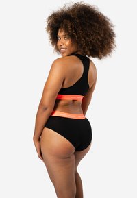 Zwarte sportbh en high-waisted onderbroek met oranje tailleband. Zachte stof, racerback ontwerp, discreet merktekst op de band.