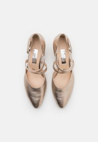 Beige metallinväriset flats kengät, joissa on terävä kärki, avoimet sivut ja nilkkahihnat. Sisäosa esittelee metallista brändäystä. Sileä nahkapinta.