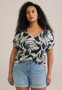 Top a maniche corte con scollo a V, caratterizzato da un motivo di foglie blu navy, beige e crema, abbinato a pantaloni shorts in denim azzurro chiaro con risvolti.