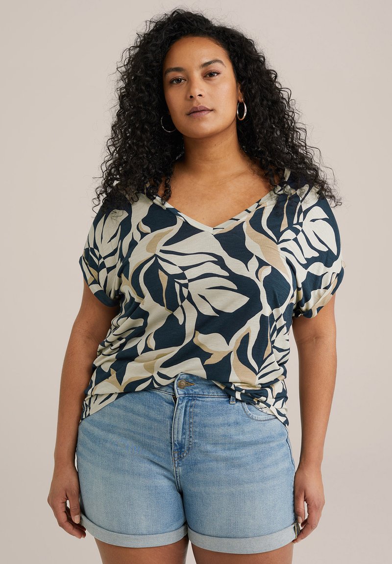 Top a maniche corte con scollo a V, caratterizzato da un motivo di foglie blu navy, beige e crema, abbinato a pantaloni shorts in denim azzurro chiaro con risvolti.