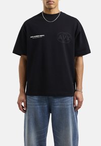 Camiseta de algodón negra con un ajuste holgado, que presenta un logo y texto en blanco en la parte frontal, y un logo tonal sutil en la parte trasera.