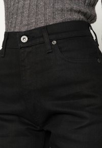 Jeans de mezclilla negra con un diseño ajustado, que cuentan con un cierre de botón metálico, bolsillos laterales y detalles de costura sutiles.