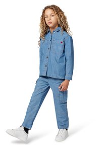 Tenue en denim composée d'une veste boutonnée bleu clair et d'un pantalon assorti, avec des poches avant et des baskets blanches.