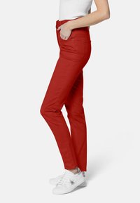Jeans ajustados rojos hechos de tejido elástico, con cintura alta, bolsillos laterales y una textura suave, combinados con zapatillas blancas.