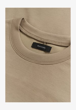 Bež majica s okruglim izrezom, s dvostrukim prošivenim šavom na ovratniku i crnim logom marke "Matinique" ušivenim unutar ovratnika.