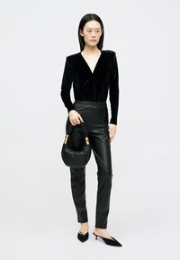 Fekete bársony body mély V-nyakkal, magas derekú fekete műbőr nadrággal és egy kis fekete kézitáskával, aranyszínű fém kiegészítőkkel párosítva.