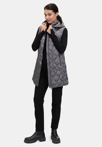 Szary pikowany kamizelka z kapturem, z zapięciem na zamek i bocznymi kieszeniami. Nosi się ją na czarnej bluzce i spodniach, uzupełnioną czarnymi botkami za kostkę.