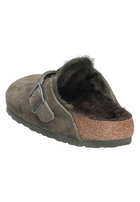Mule de ante verde con forro de piel de pelaje, plantilla de corcho y hebilla de metal ajustable. Suela texturizada para mayor agarre y comodidad.