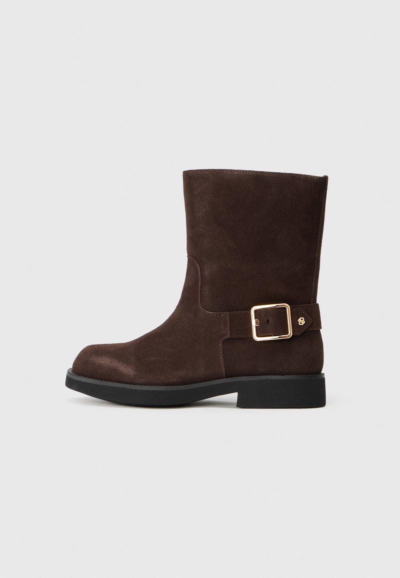 Botim de tornozelo em suede castanho com ponta arredondada, sola preta plana e detalhe de fivela dourada na lateral. Textura suave e design simples.