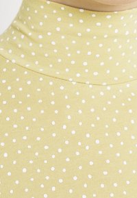 Gelbes, geripptes Rollkragenshirt mit enger Passform, das gleichmäßig verteilte weiße Pünktchen im gesamten Stoff aufweist.