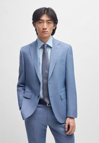 Blazer azul claro e calças combinando, fabricado com material texturizado, com lapelas recortadas, dois botões, combinado com uma camisa azul clara e uma gravata estampada.