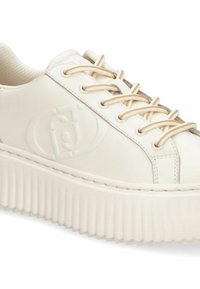 Baskets compensées blanches en matériau synthétique lisse, avec lacets plats, logo en relief et semelle rainurée pour une meilleure adhérence.