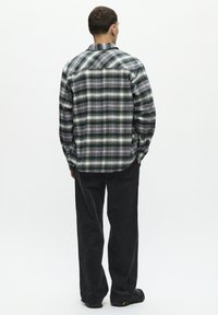 Plaid shirt in green, black, and white, long sleeves, buttoned cuffs, paired with black corduroy pants and black footwear.