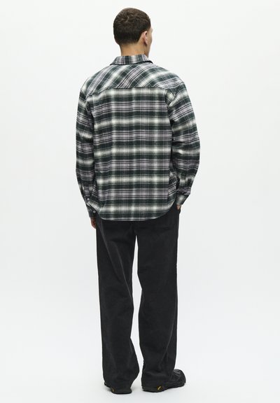 Chemise à carreaux verte, noire et blanche, à manches longues, avec des poignets boutonnés, associée à un pantalon en velours côtelé noir et des chaussures noires.