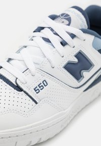 Baskets blanches et bleu marine avec une tige en cuir perforée, des lacets et un détail "550" sur le côté. Semelle en caoutchouc texturé.